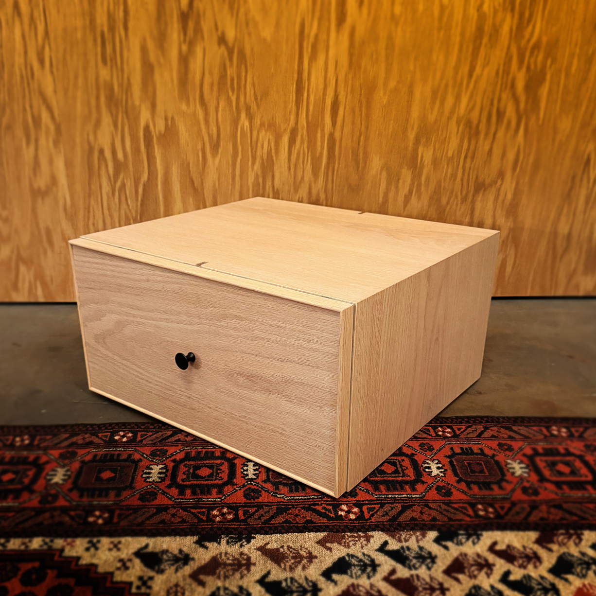 A minimalist wooden stool with a flat top and side panels on a plain background.