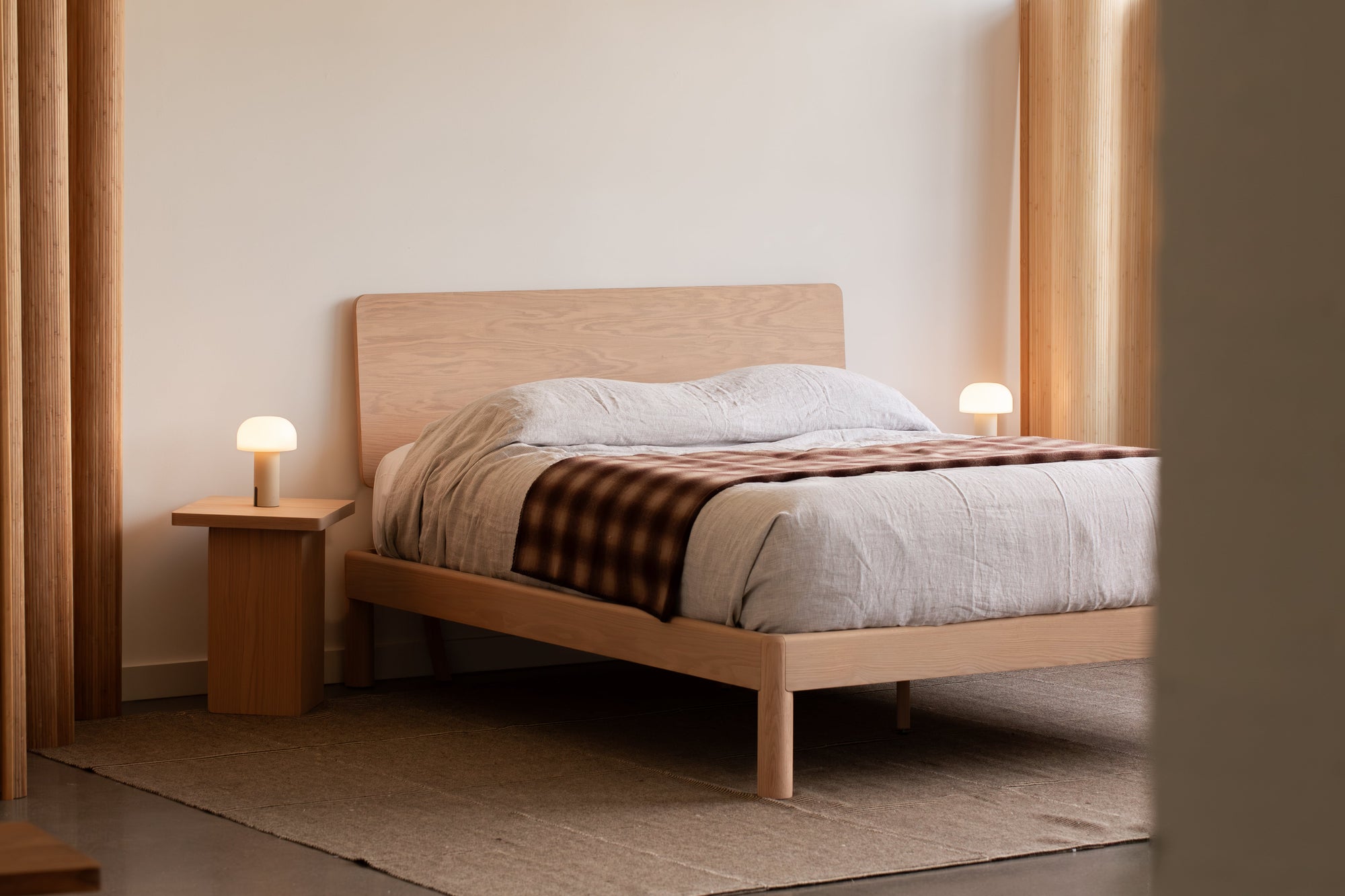 Minimalist Keeps Bolted Bed frame in light natural finish and two Keeps Nightstands with modern lights and checkered blanket in contemporary bedroom