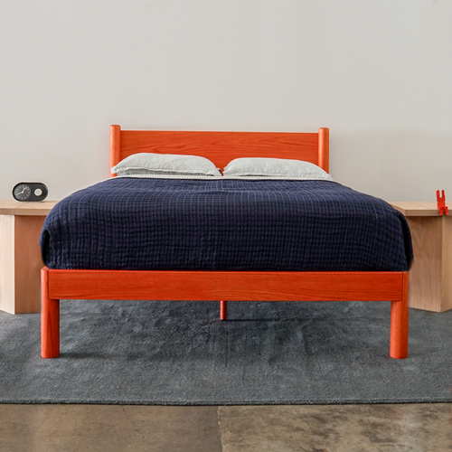 Custom Color modern solid oak designer bed frame Keeps Architect bed with headboard integrated joinery in bright red vermillion with navy duvet and blue sheets with Keeps Nightstands in light natural finish against white wall on blue carpet