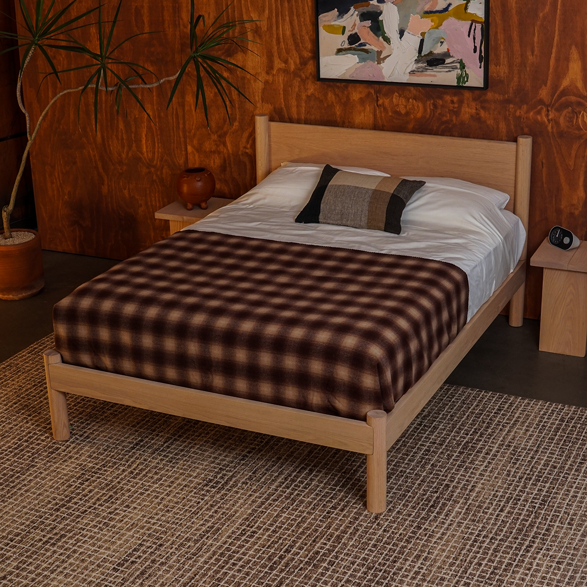 Keeps Architect oak bed frame in natural finish with plaid blanket in a cozy room with wooden walls, spiky plant, two natural keeps nightstands, and checked rug.