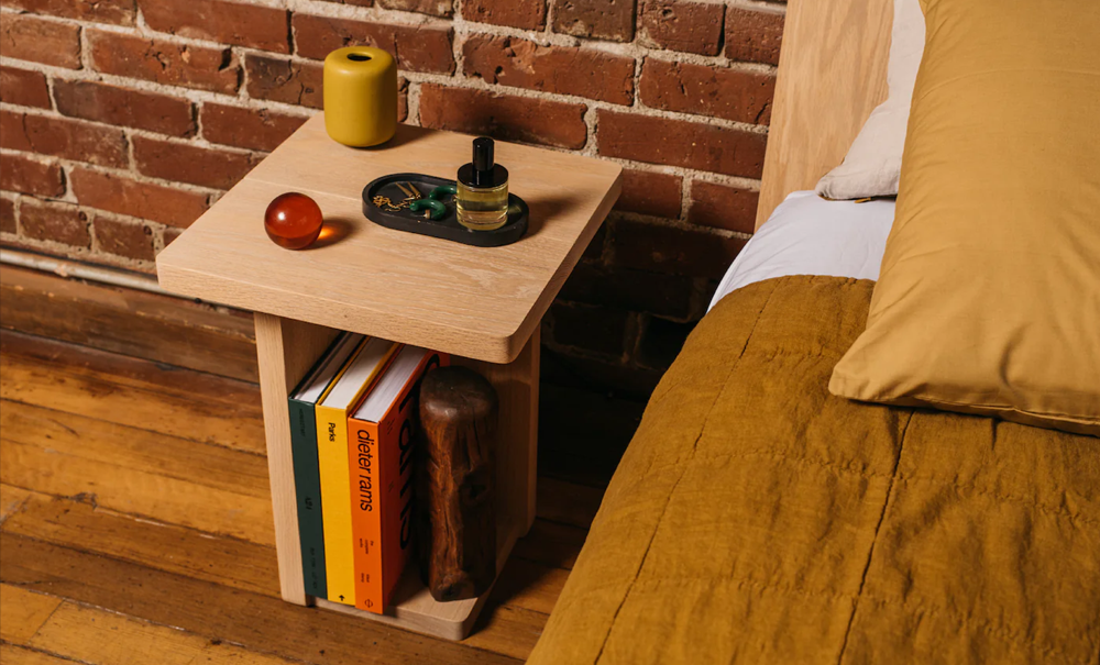 Keeps Modern Minimal Nightstand in Natural finish next to bed with books next to brick wall
