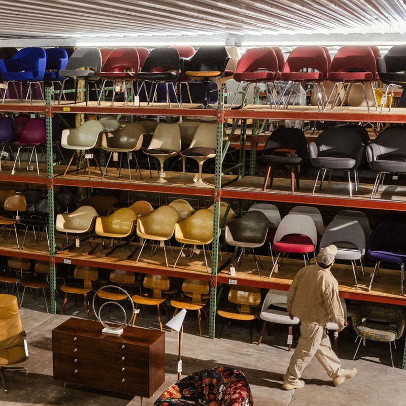 Rarify collection studio with shelves filled with iconic design, vintage chairs and a person walking by.