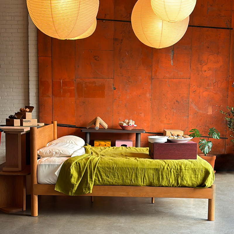 Keeps solid oak architect bed frame and headboard in honey stain with green bedding, and pendant lights on a rust wall.