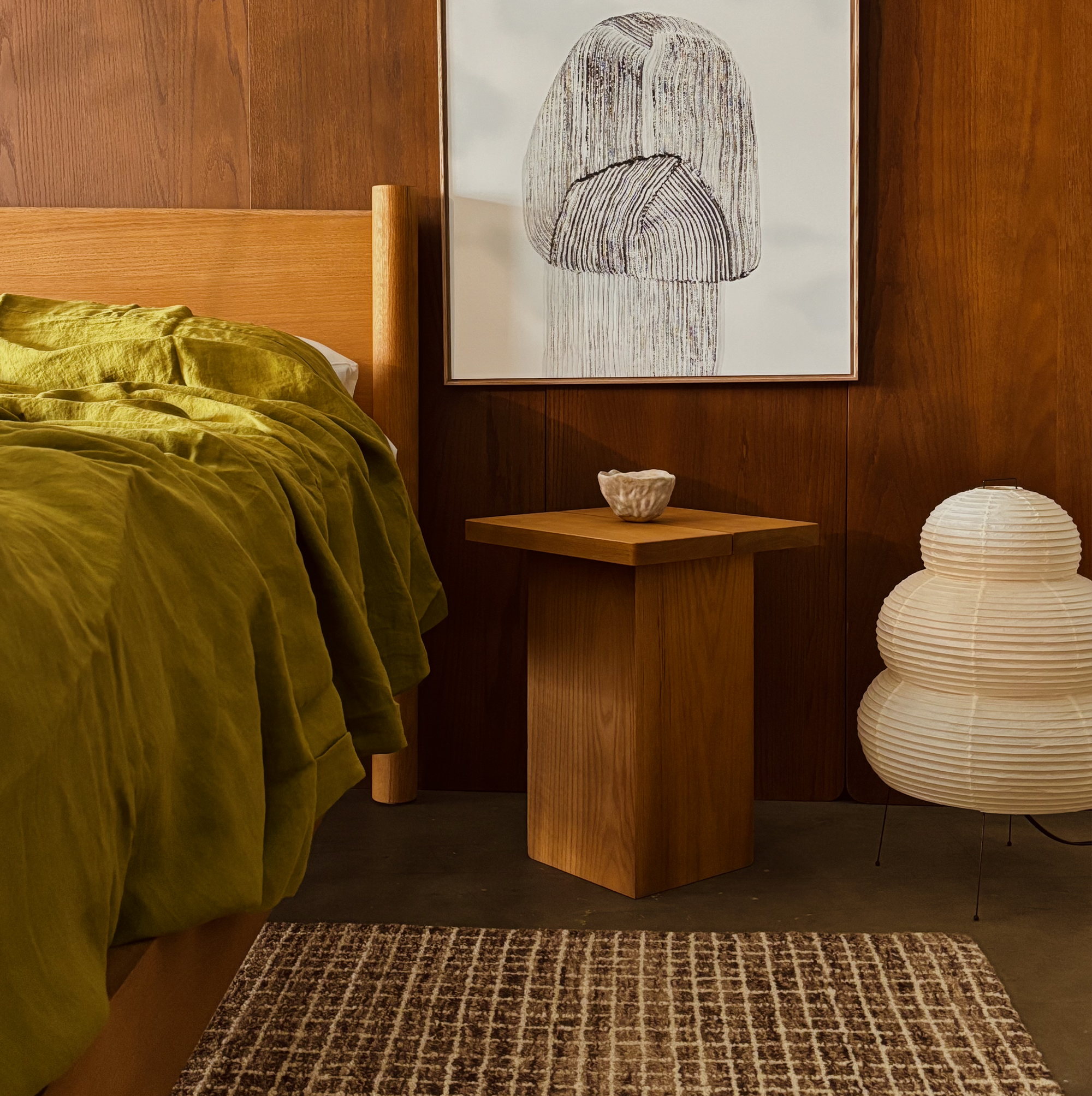 Keeps oak Architect bed frame and headboard in honey finish with green sheets, Keeps honey nightstand, abstract art on a wood wall, and an akari lamp
